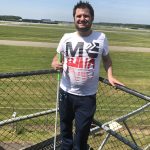 Ekrem staat met een taststok op een verhoging, bij Luchtvaartmuseum Aviodrome in Lelystad. Achter hem de start- en landingsbaan van luchthaven Lelystad